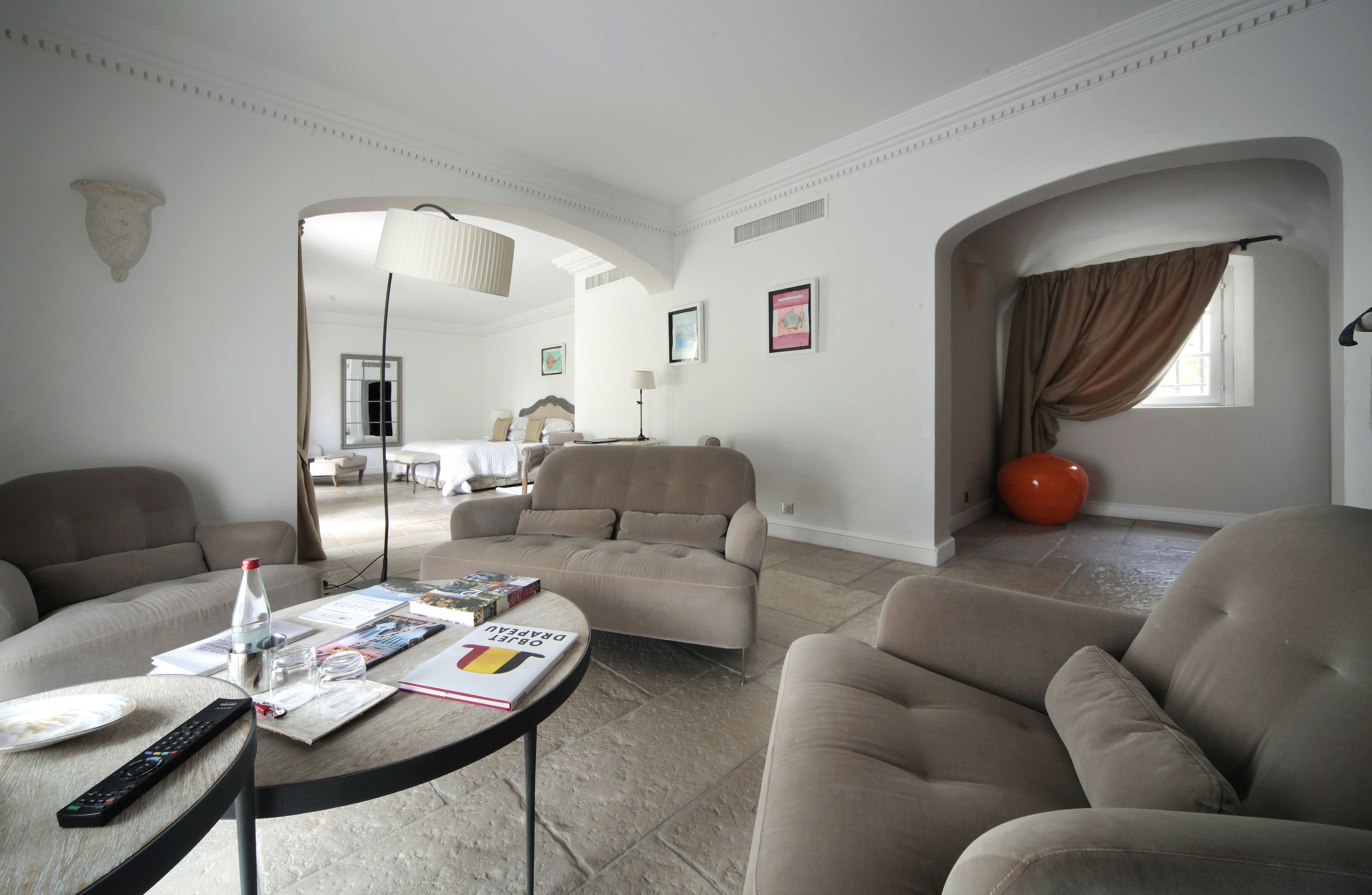 A spacious living area with a sofa, armchairs, and a coffee table. There is a remote control and a book on the table.