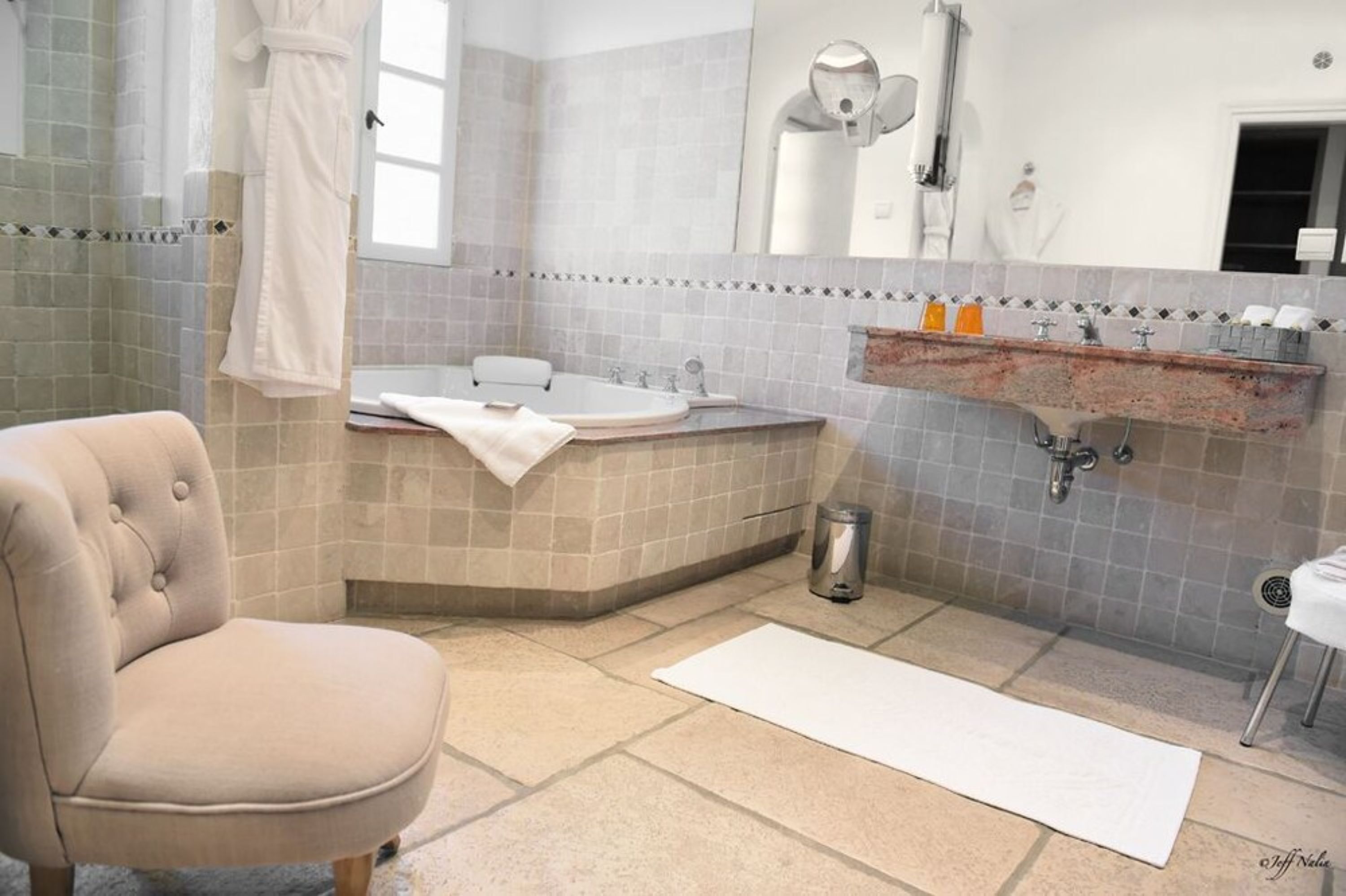 A bathroom with a bathtub, a sink, a mirror, and a chair.
