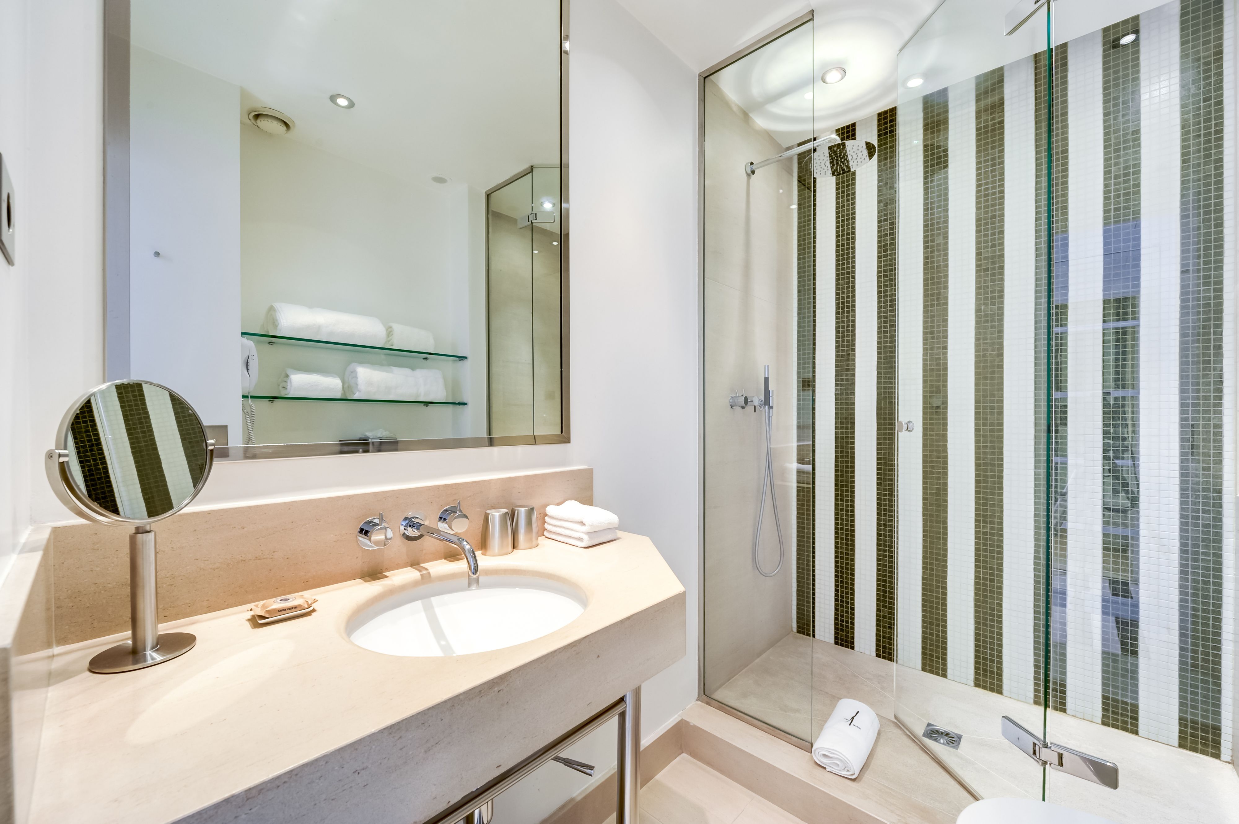 A modern bathroom with a large mirror, a sink, and a glass-enclosed shower.