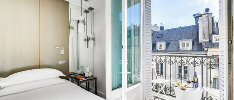 Habitación de hotel con cama, mesita de noche y vista del paisaje urbano a través de un ventanal grande.