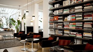 A modern library with bookshelves, comfortable seating, and a large window. - Hotel Le A (Paris)