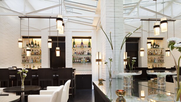 A modern bar area with white brick walls, hanging pendant lights, and a glass display case with bottles. - Hotel Le A (Paris)