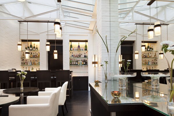 Een moderne bar met witte bakstenen muren, hangende pendelverlichting en een glazen displaykast met flessen.