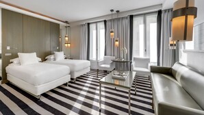 A modern hotel room with two beds, a sofa, a glass coffee table, and large windows with curtains. - Hotel Le A (Paris)
