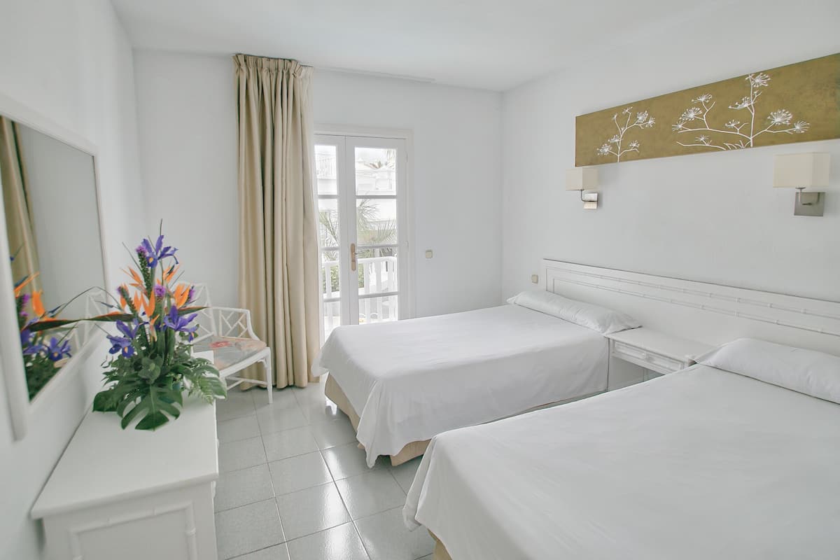A hotel room with two beds, a desk, a chair, and a window with curtains.