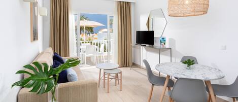A modern living room with a sofa, a coffee table, a dining table with chairs, a TV, and a large window with curtains.