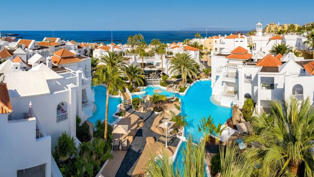 Un resort con una piscina grande, edificios blancos y palmeras.