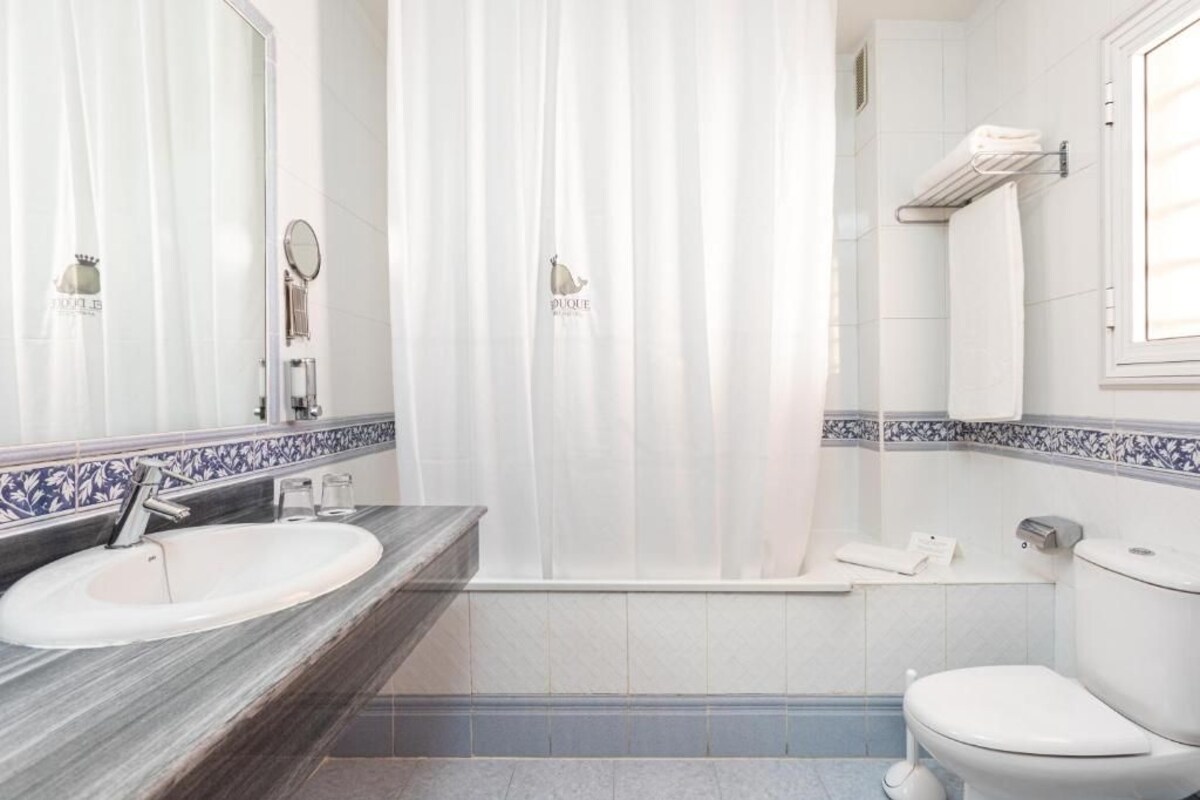 A bathroom with a white sink, a mirror, a shower curtain, a toilet, and a towel rack.