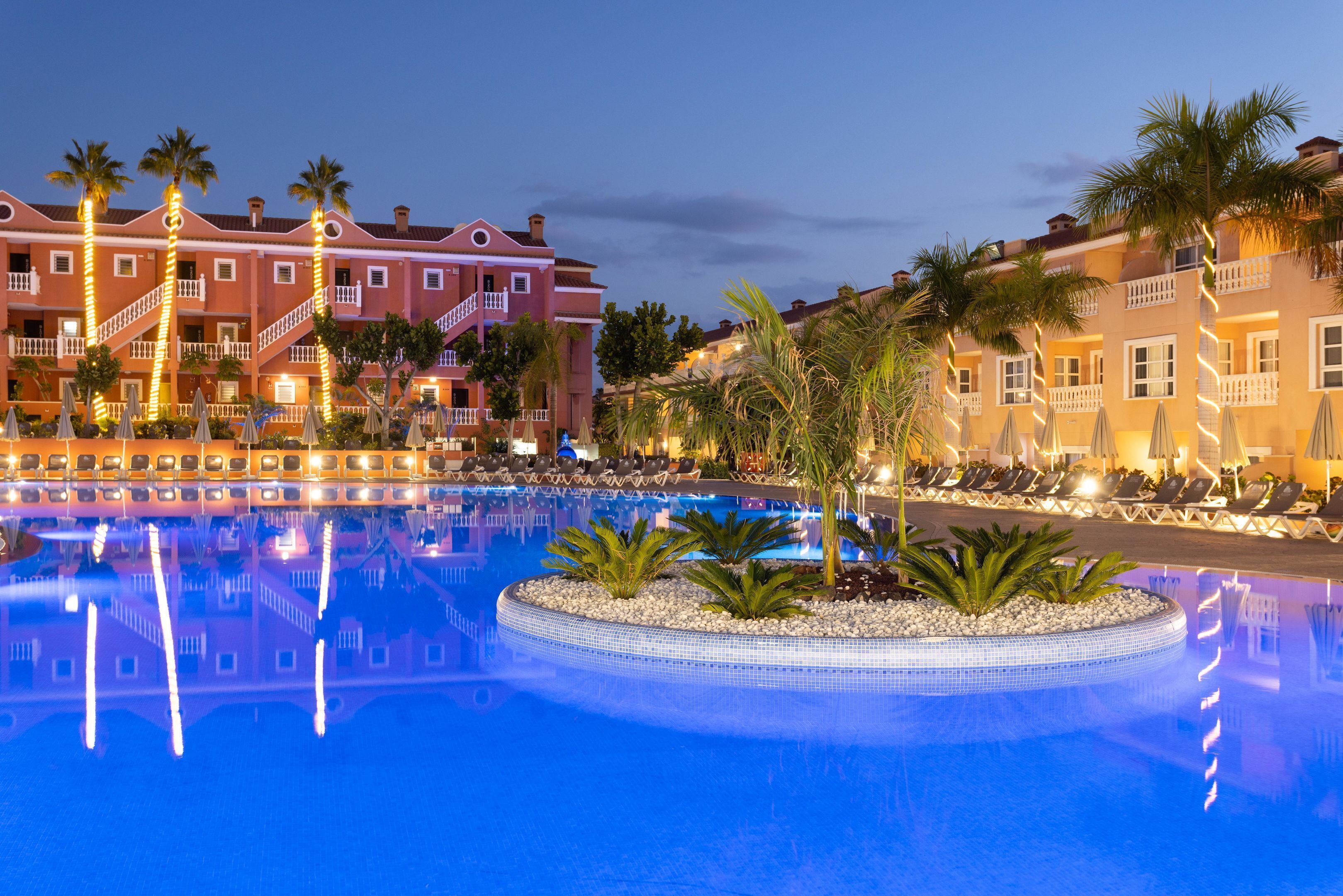 A hotel with a pool, palm trees, and a well-lit building facade.