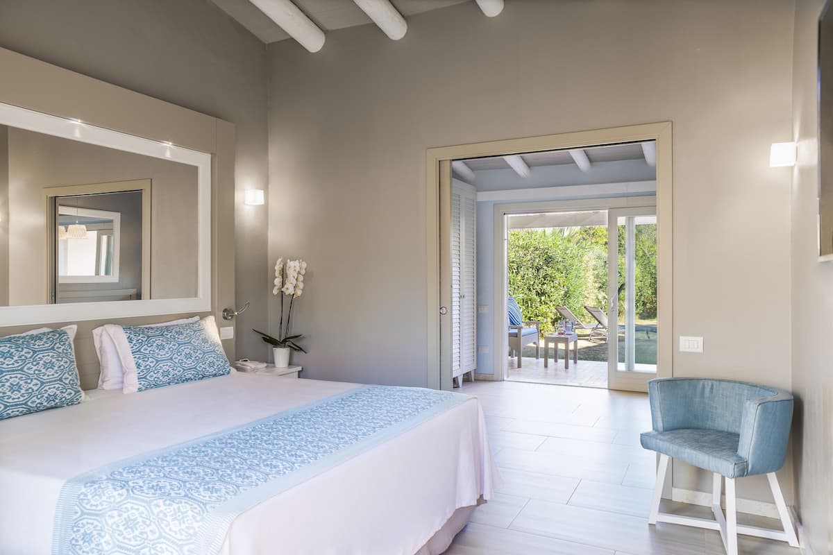 A bedroom with a bed, a chair, a mirror, and a door leading to an outdoor area.
