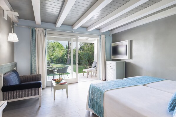 A modern hotel room with a bed, a sofa, a TV, and a balcony with a view of the garden.