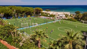 Um campo de futebol com balizas, rodeado por palmeiras e vista para o oceano.
