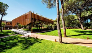 Un bâtiment moderne doté d’une façade en bois et d’une entrée en verre, entouré d’une pelouse bien entretenue et d’arbres.