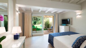 Une chambre d’hôtel avec un lit, une télévision, un bureau avec une lampe et une vue sur le jardin, visible à travers la porte-fenêtre coulissante.