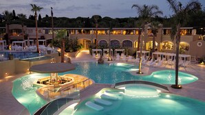 Un espace piscine dans un complexe hôtelier comprenant plusieurs piscines, des chaises longues et un bar.