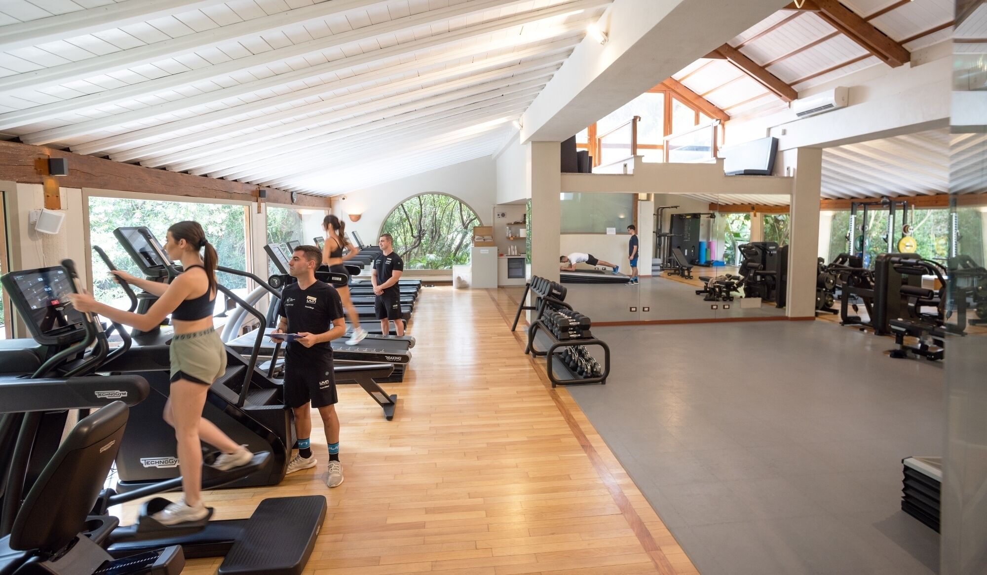 Un gimnasio con cintas de correr, pesas y un muro de espejos.