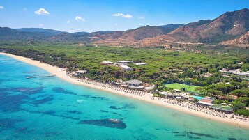 Un resort costero con villas frente a la playa, una playa de arena y abundante vegetación.