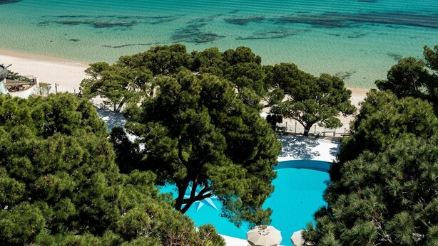An aerial view of a beach resort with a swimming pool surrounded by trees, overlooking a clear blue sea. - Forte Village Resort - Il Castello (Pula)