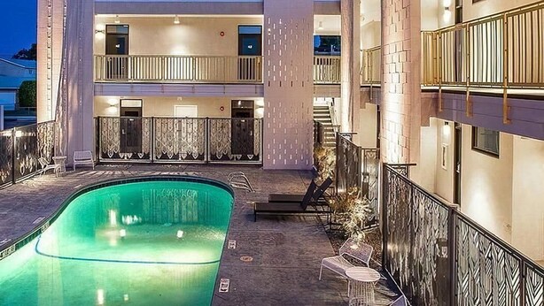 A modern building with a swimming pool, balconies, and a well-lit entrance. - The Monterey Motel (Albuquerque)