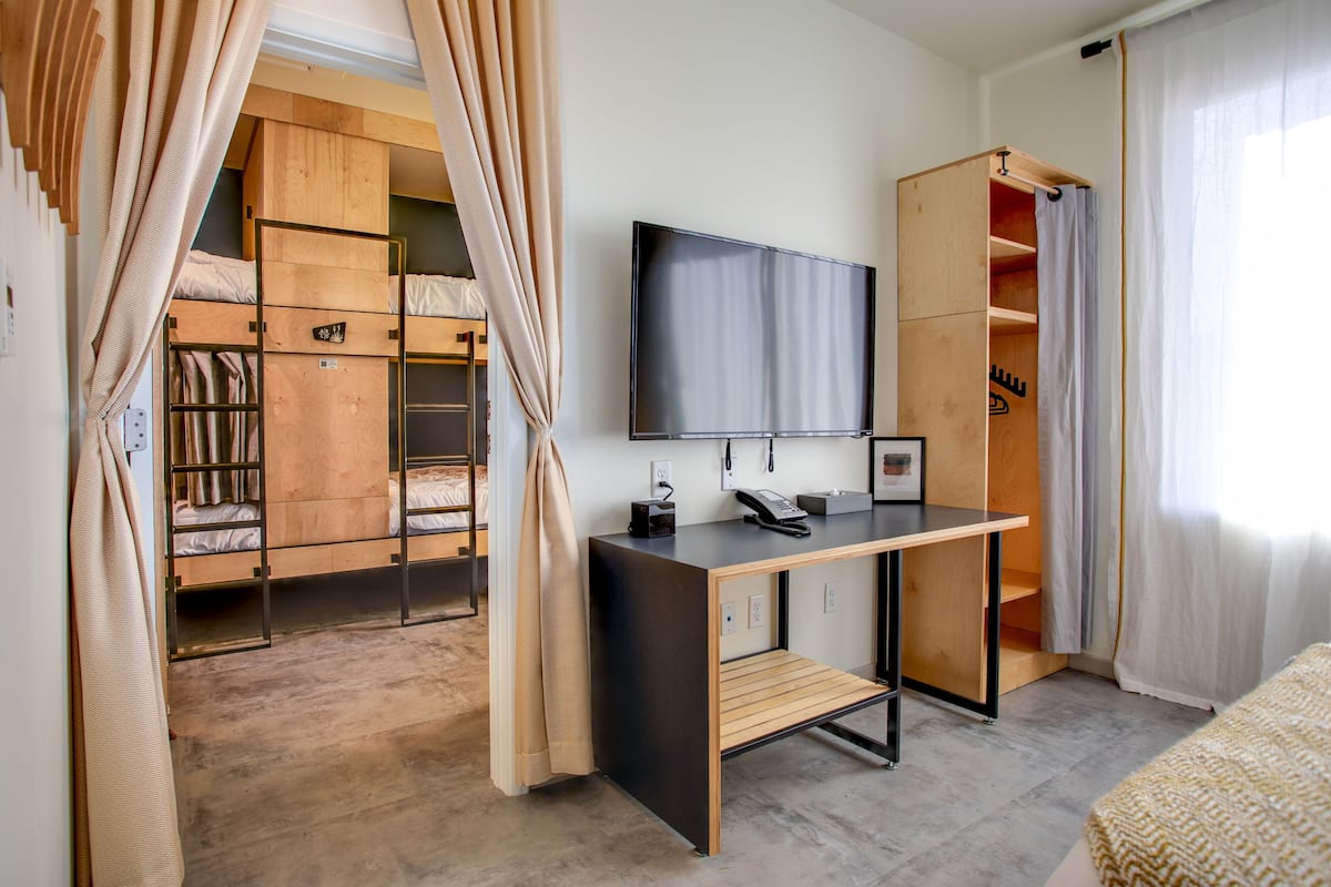 A bedroom with a bunk bed, a desk with a flat-screen TV, and a wardrobe.