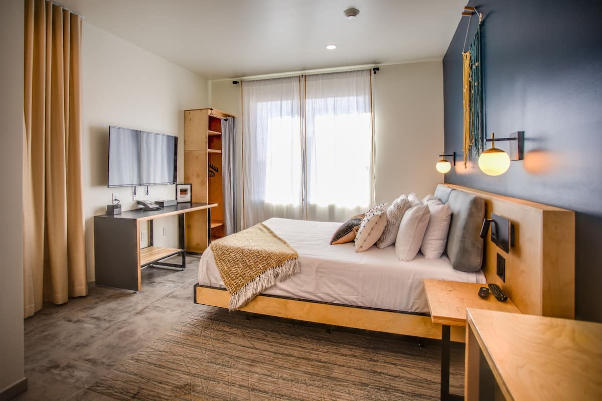 A modern hotel room with a bed, desk, and wardrobe.