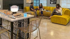 A modern lounge area with a yellow sofa, a table with a lamp, and a decorative wall panel. - The Monterey Motel (Albuquerque)