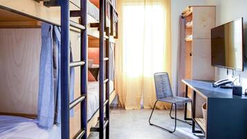 Quarto estilo dormitório com beliches, escrivaninha, cadeira, televisão e guarda-roupa.