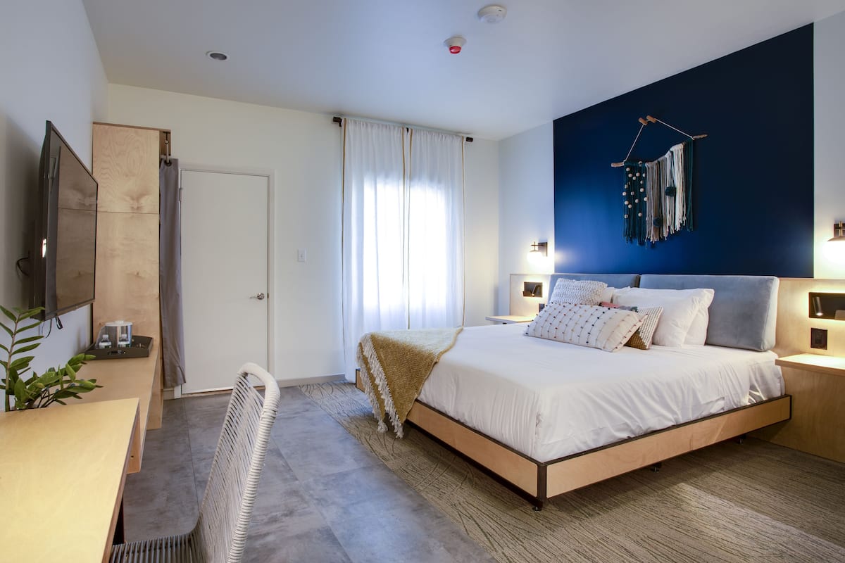 A modern bedroom with a bed, bedside tables, a TV, and a large wall art piece.