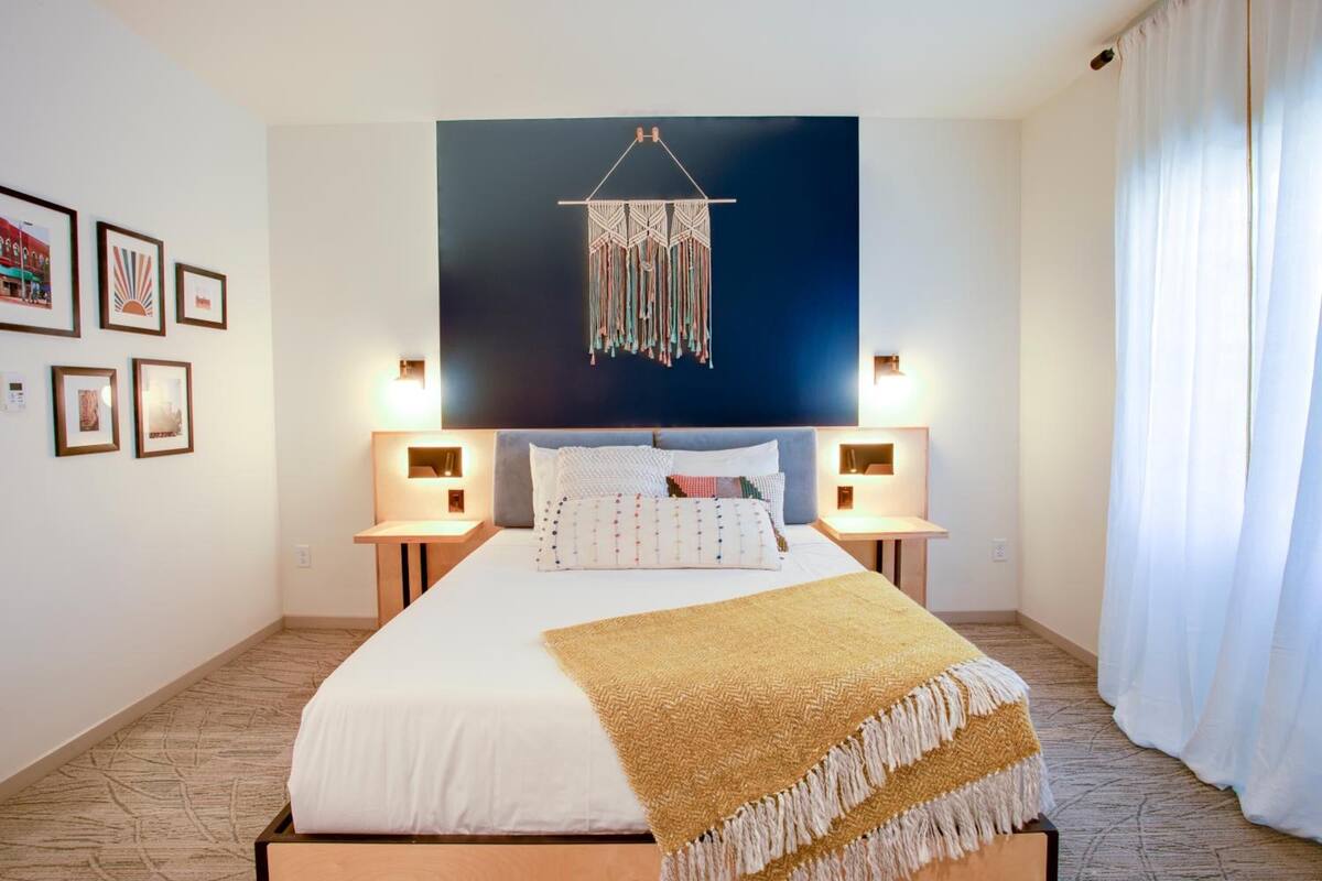 A neatly arranged hotel room with a large bed, bedside lamps, a wall-mounted artwork, and framed pictures on the wall.