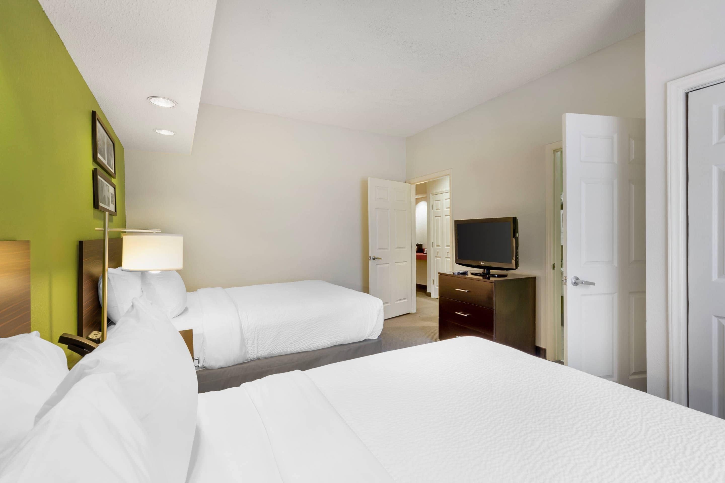 A hotel room with two beds, a television, a desk, and a mirror.