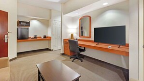 A hotel room with a kitchenette, a desk, a chair, a television, and a mirror.
