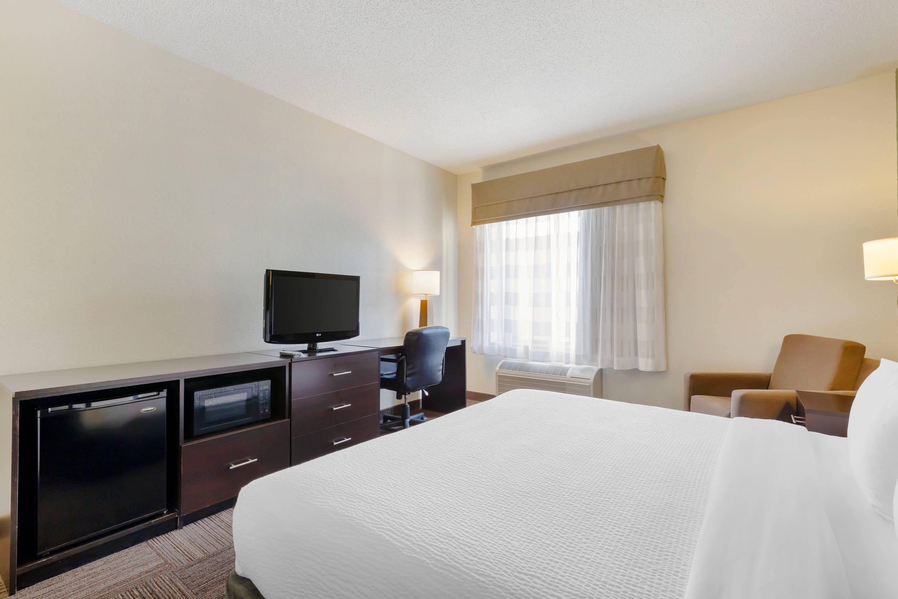 A hotel room with a bed, a desk with a television, a chair, a lamp, and a window with curtains.