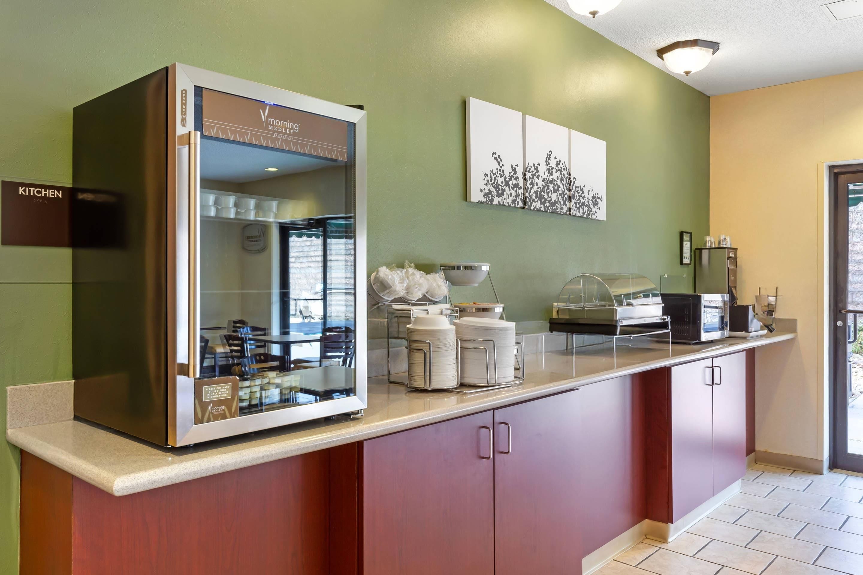 Un área de cocina moderna con un refrigerador de puerta de vidrio, microondas y una estación para café.