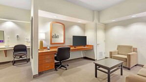 A hotel room with a desk, chair, sofa, and a television.