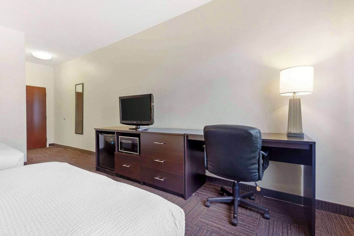 Een hotelkamer met een bed, een bureau met een computer en een lamp, en een stoel.