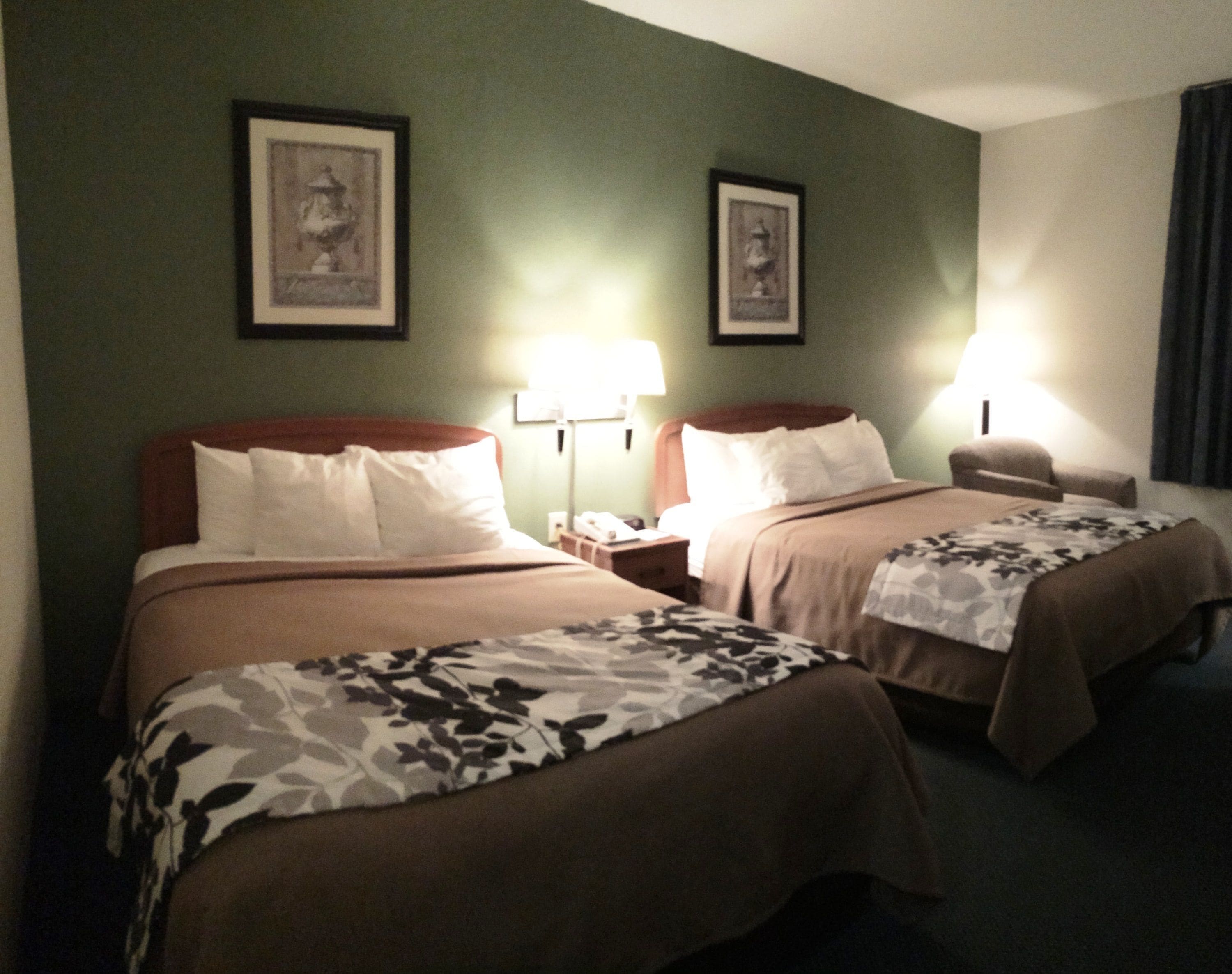 Habitación de hotel con dos camas, cada una con cabecera, mesitas de noche, lámparas y cuadros en la pared.