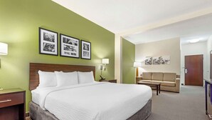 A hotel room with a large bed, a nightstand, a desk, a sofa, and a wall with framed pictures.