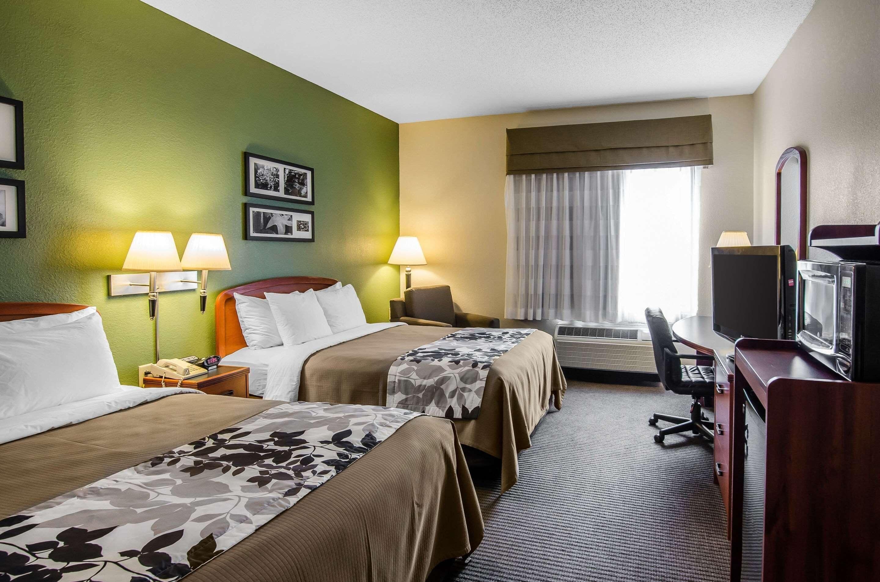 A hotel room with two beds, a desk, a television, and a window with curtains.