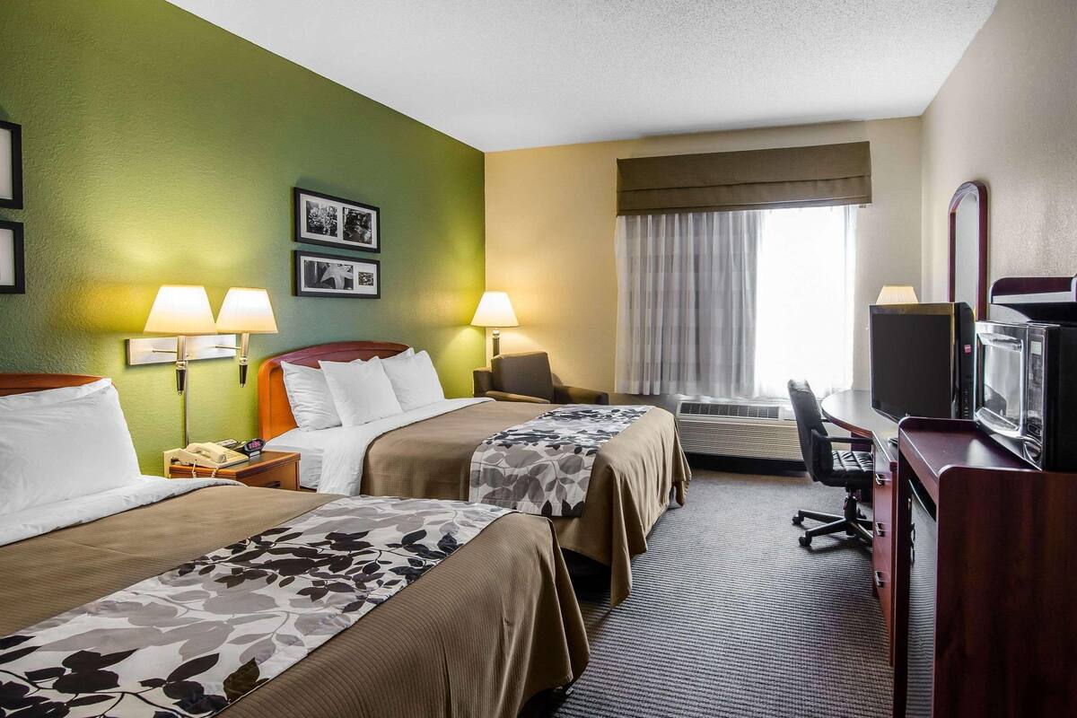 Een hotelkamer met twee bedden, een bureau, een televisie en een raam met gordijnen.