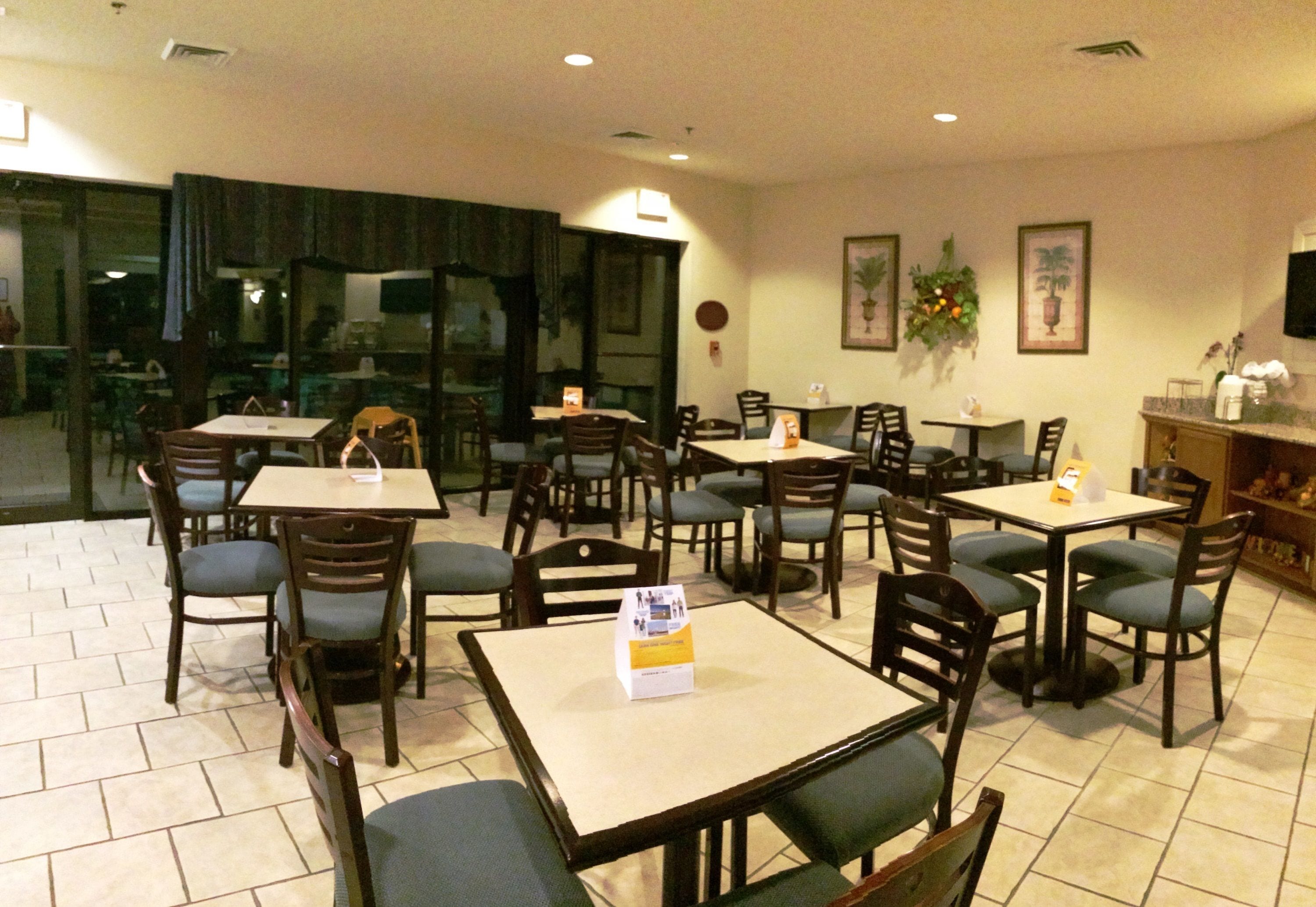 A restaurant with multiple tables and chairs, a tiled floor, and a view through the glass door.