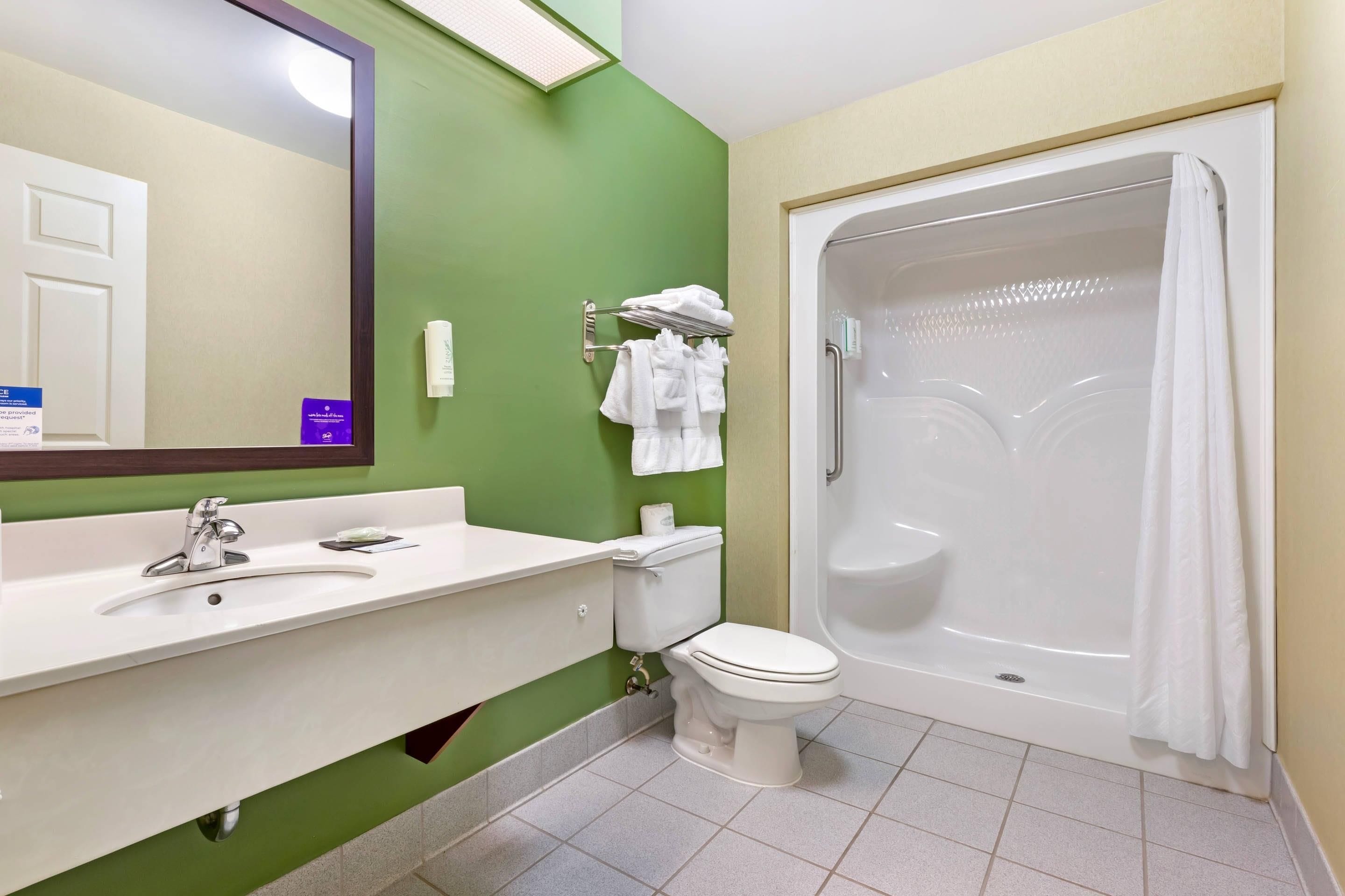 Ein Badezimmer mit grüner Wand, Waschbecken in Weiß, Toilette und Badewanne in Weiß.