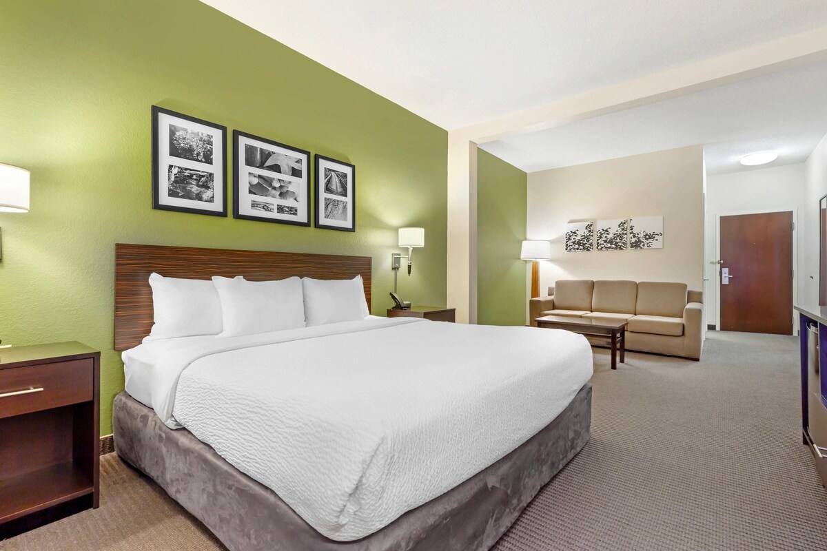 A hotel room with a large bed, a desk, a sofa, and a wall with framed pictures.