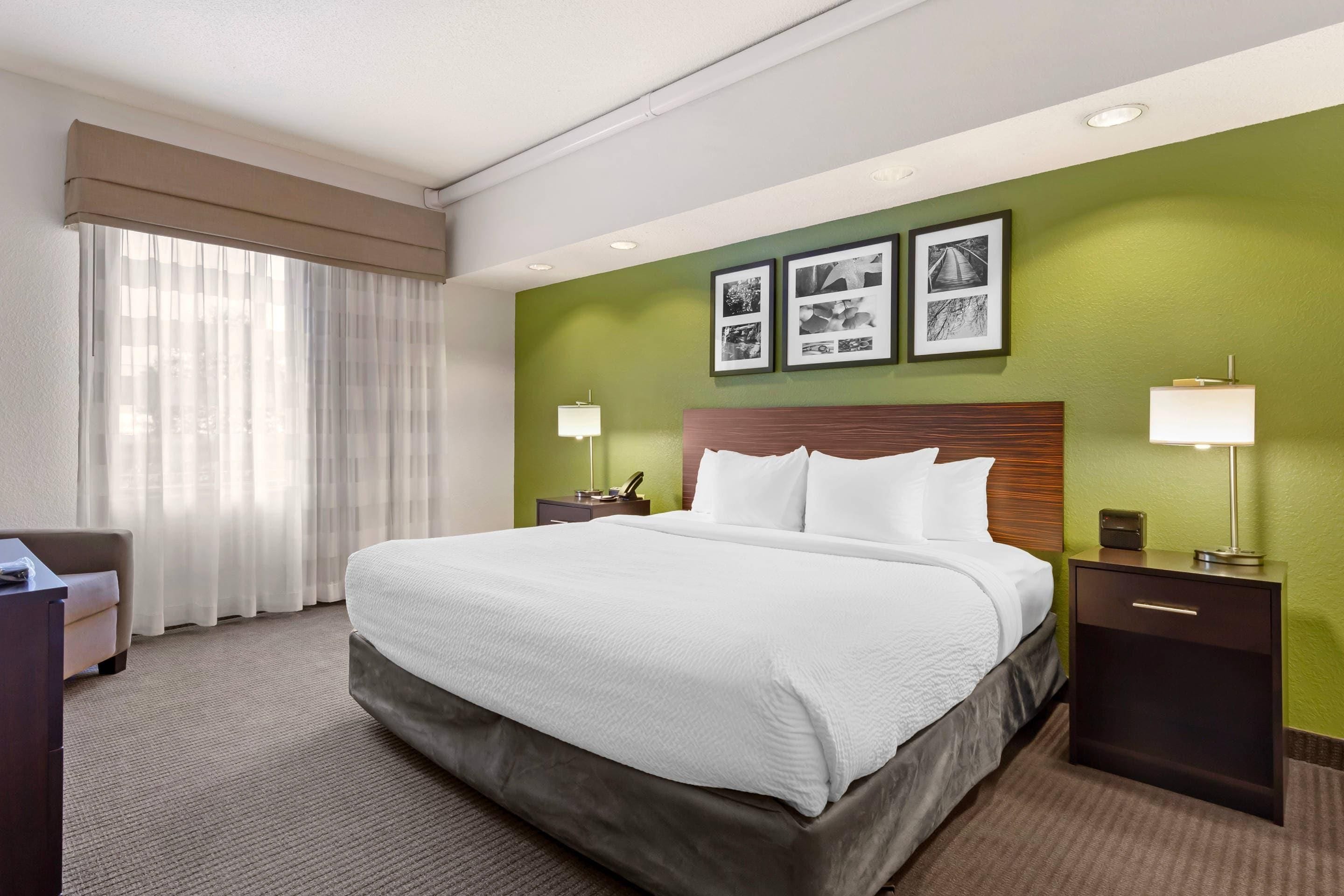 Habitación de hotel con una cama grande, dos mesitas de noche, un escritorio y una silla. Hay tres cuadros enmarcados en la pared.