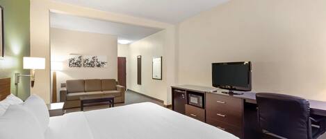 A hotel room with a bed, a desk with a computer, a chair, a television, and a sofa.