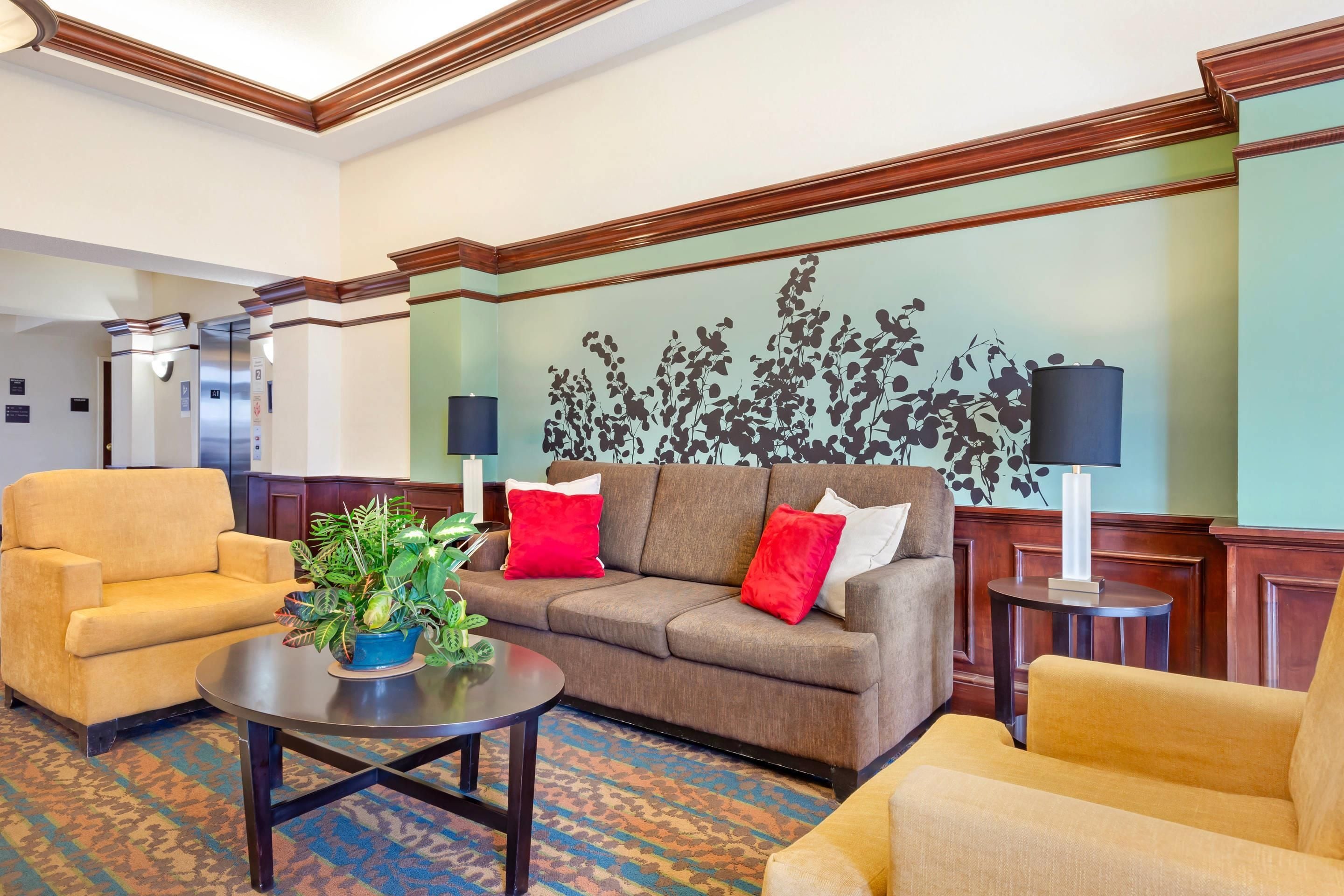 Un hall d’hôtel avec un canapé marron, deux fauteuils, une table basse ornée d’une plante et un mur décoré d’une fresque florale.