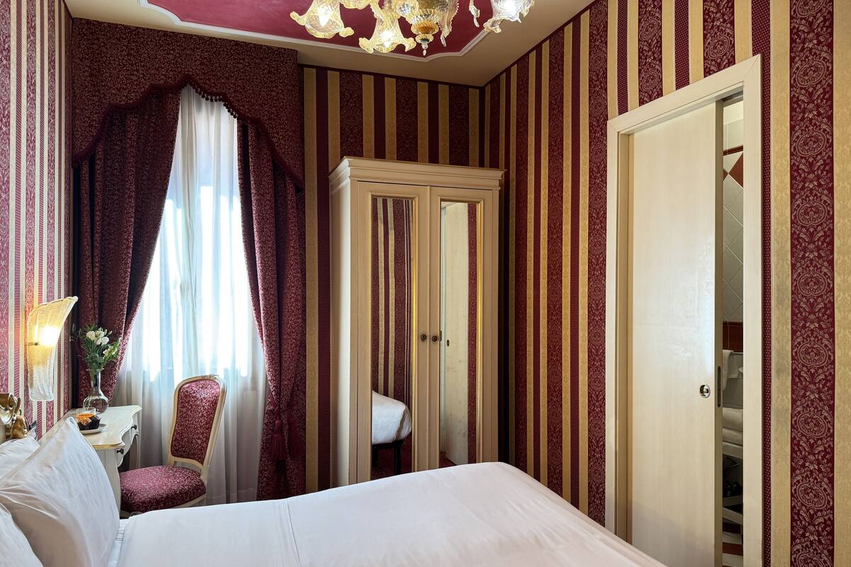 Una habitación de hotel con una cama grande, un armario, un escritorio con lámpara y una silla.
