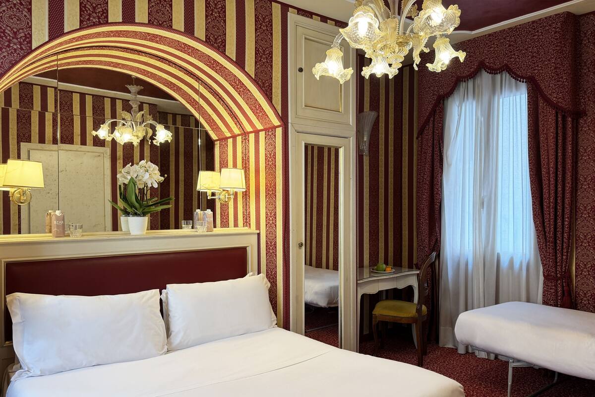 Una habitación de hotel con una cama grande, una zona de estar, una tocador con espejo y una araña.