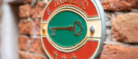 Una señal circular con el texto "TINTORETTO" y un símbolo de llave, colocada sobre una pared de ladrillo.