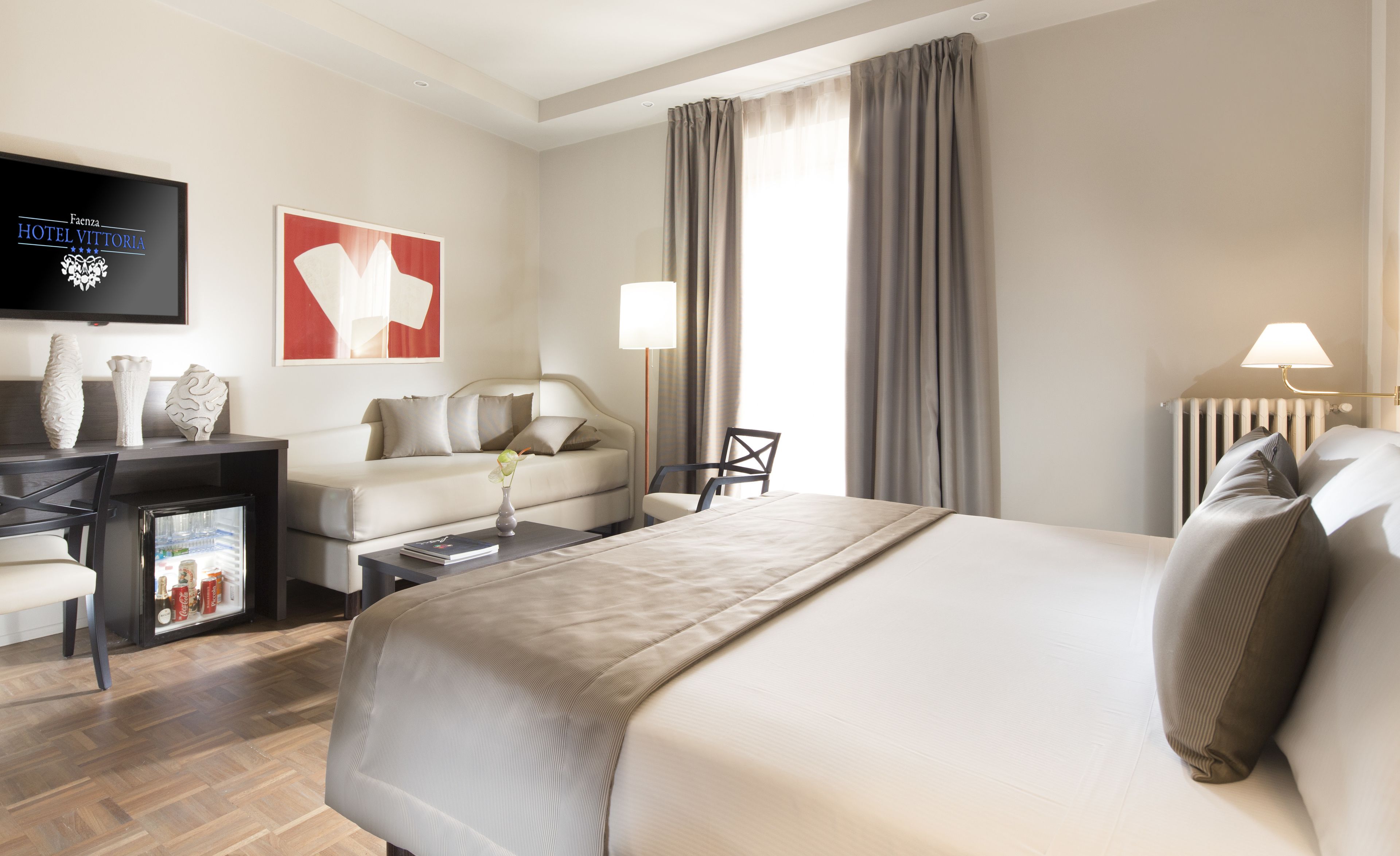 A hotel room with a large bed, a desk with a computer, a chair, a coffee table, and a TV mounted on the wall.
