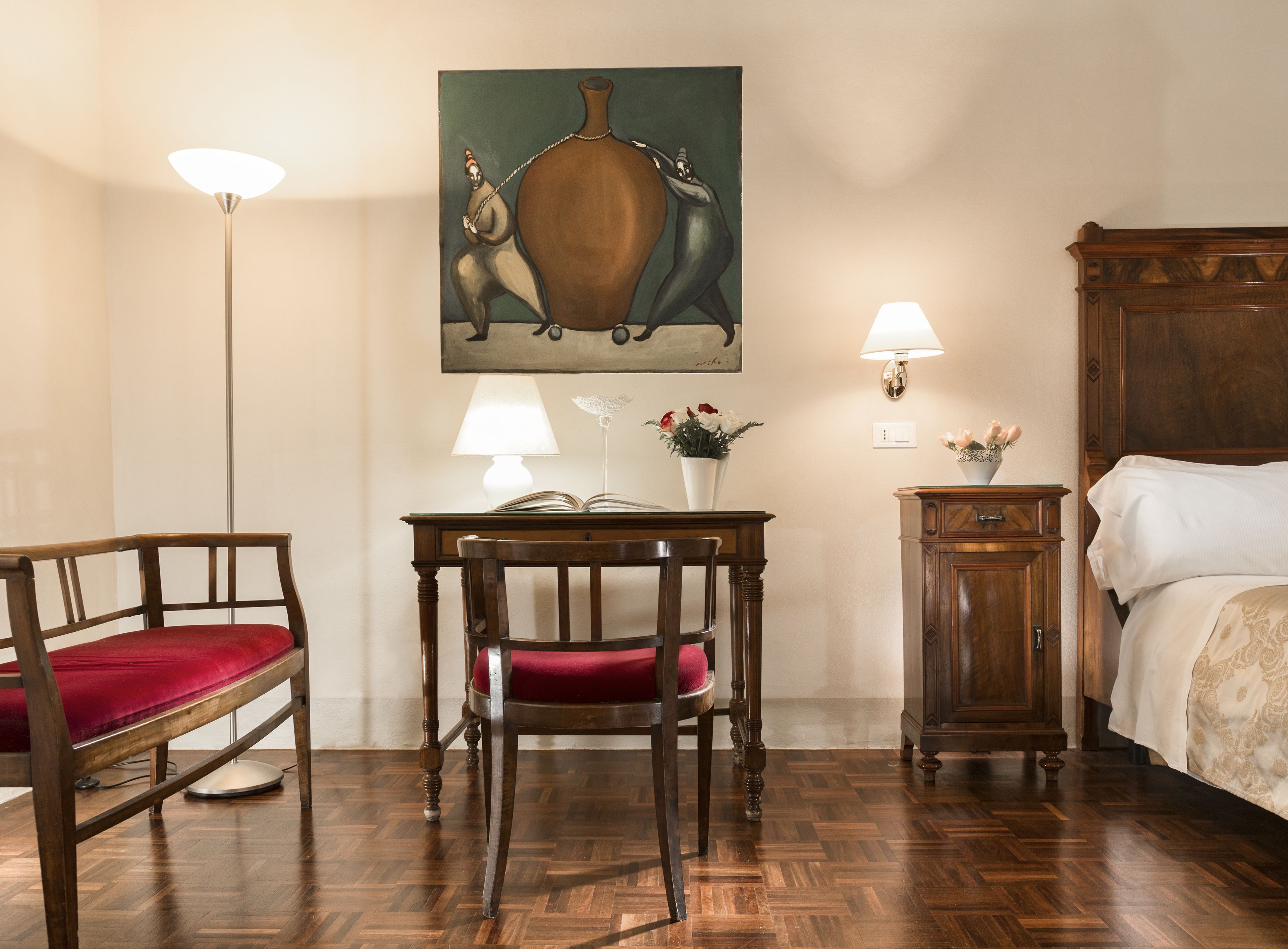 Habitación de hotel con una cama de madera, un escritorio con una silla, una lámpara de pie y un cuadro en la pared.